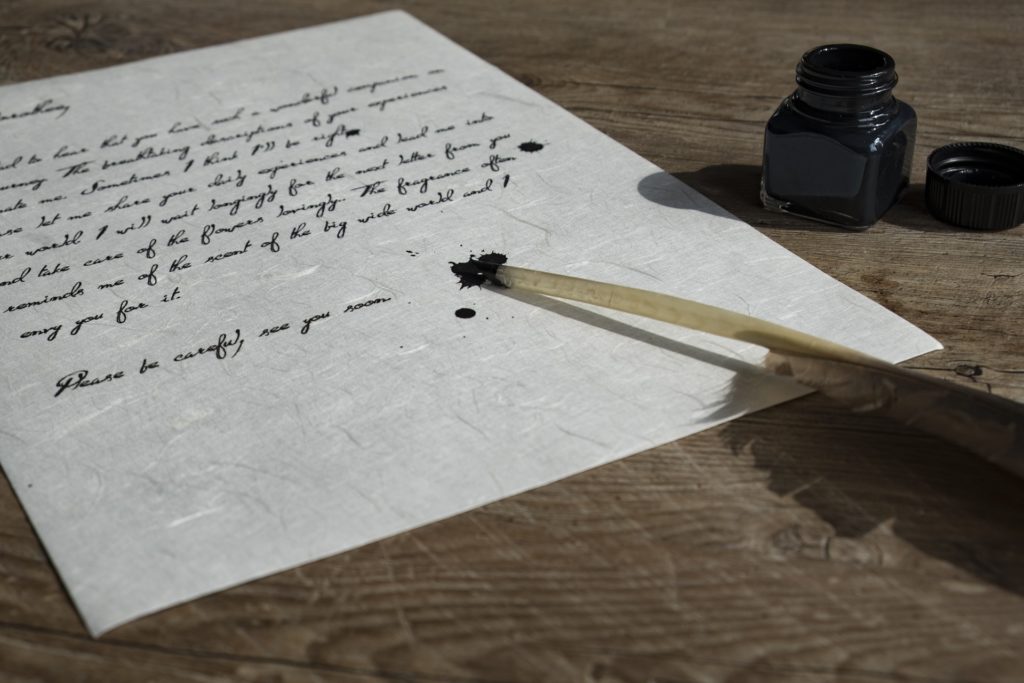 Imagen de hoja de papel pergamino, un frasco de tinta y una pluma que ha dejado dos manchas sobre el papel