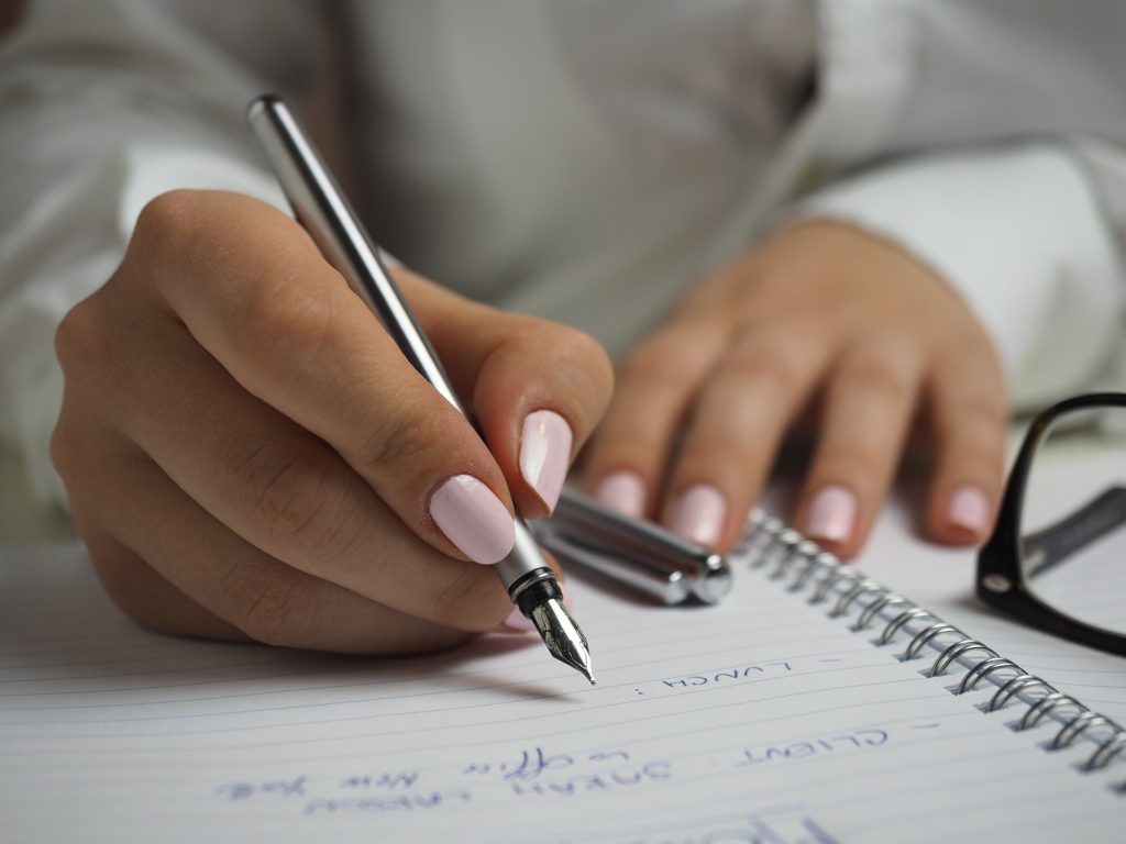 Imagen de unas manos que sostienen un estilógrafo con el cual está escribiendo sobre un cuaderno argollado