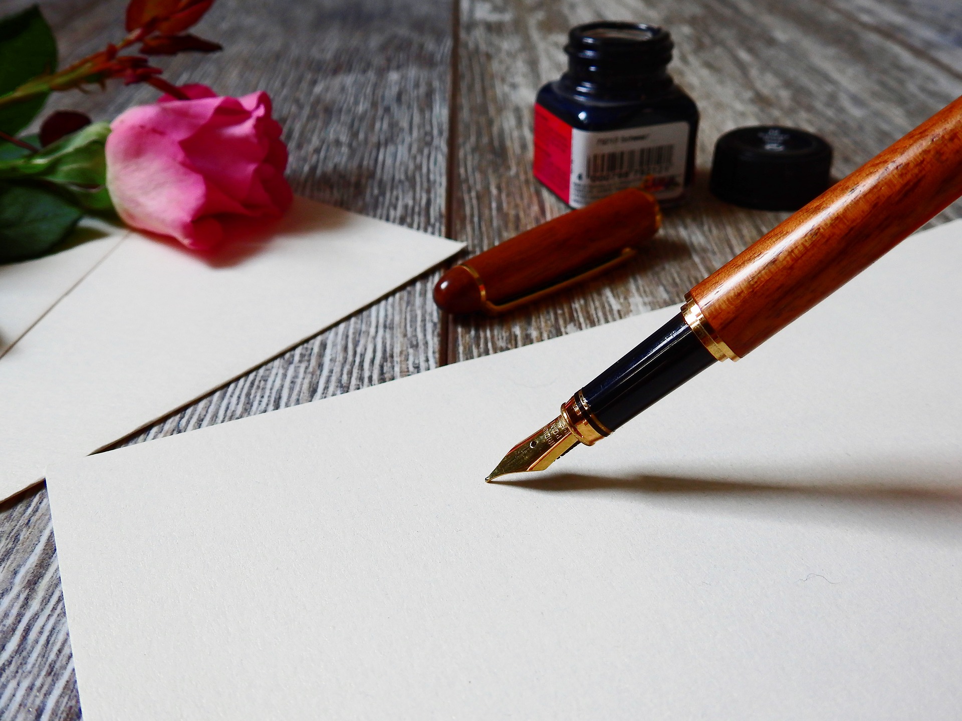 imagen de un estilógrafo sobre una hoja de papel pergamino en blanco, un frasco de tinta y una flor