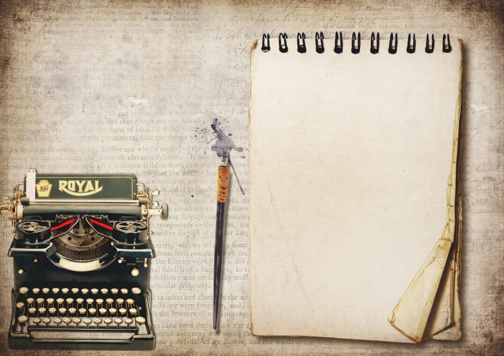 Imagen de una vieja máquina de escribir, una pluma y un viejo cuaderno de notas